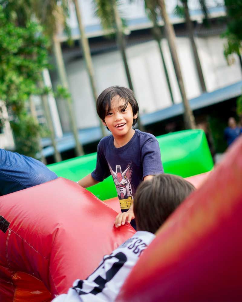 A young boy in a blue shirt is sitting on a red inflatable couch.
