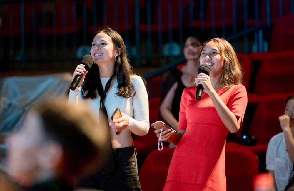 Two women are singing into microphones in front of a crowd.