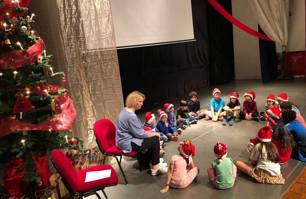 A group of children are sitting in a circle in front of a christmas tree.