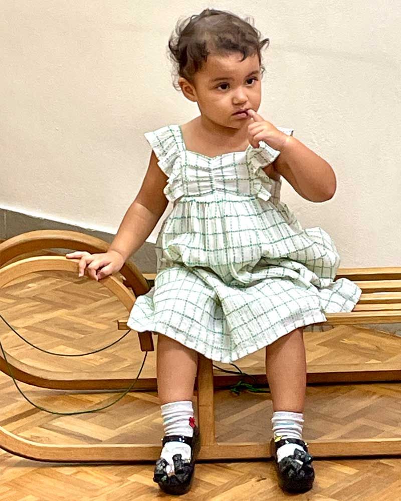 A little girl in a dress is sitting on a wooden sled.