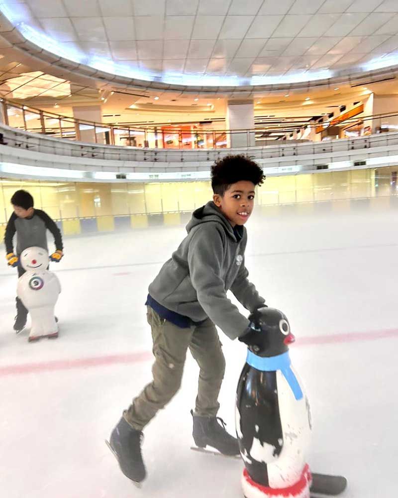 A young boy is ice skating with a penguin and a snowman.