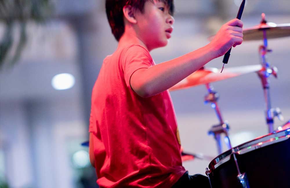A young boy in a red shirt is playing drums on a stage.
