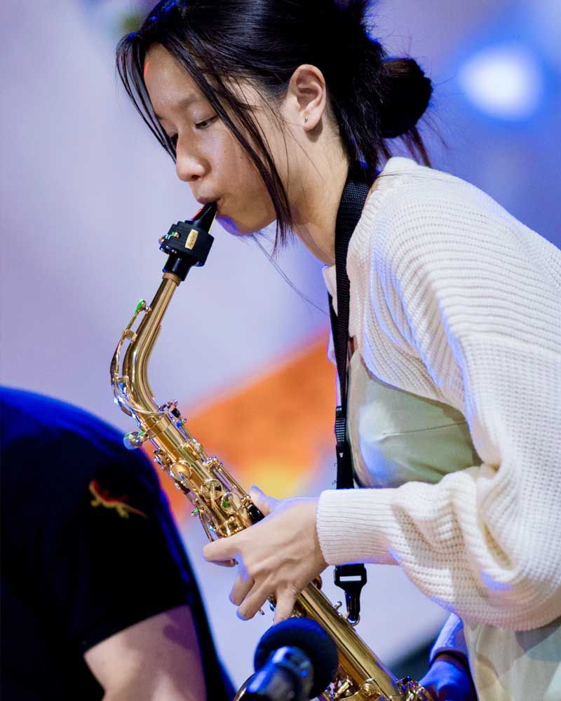 A woman in a white sweater is playing a saxophone