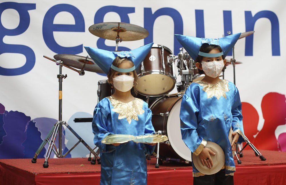 Two girls wearing masks are standing on a stage in front of a drum set.