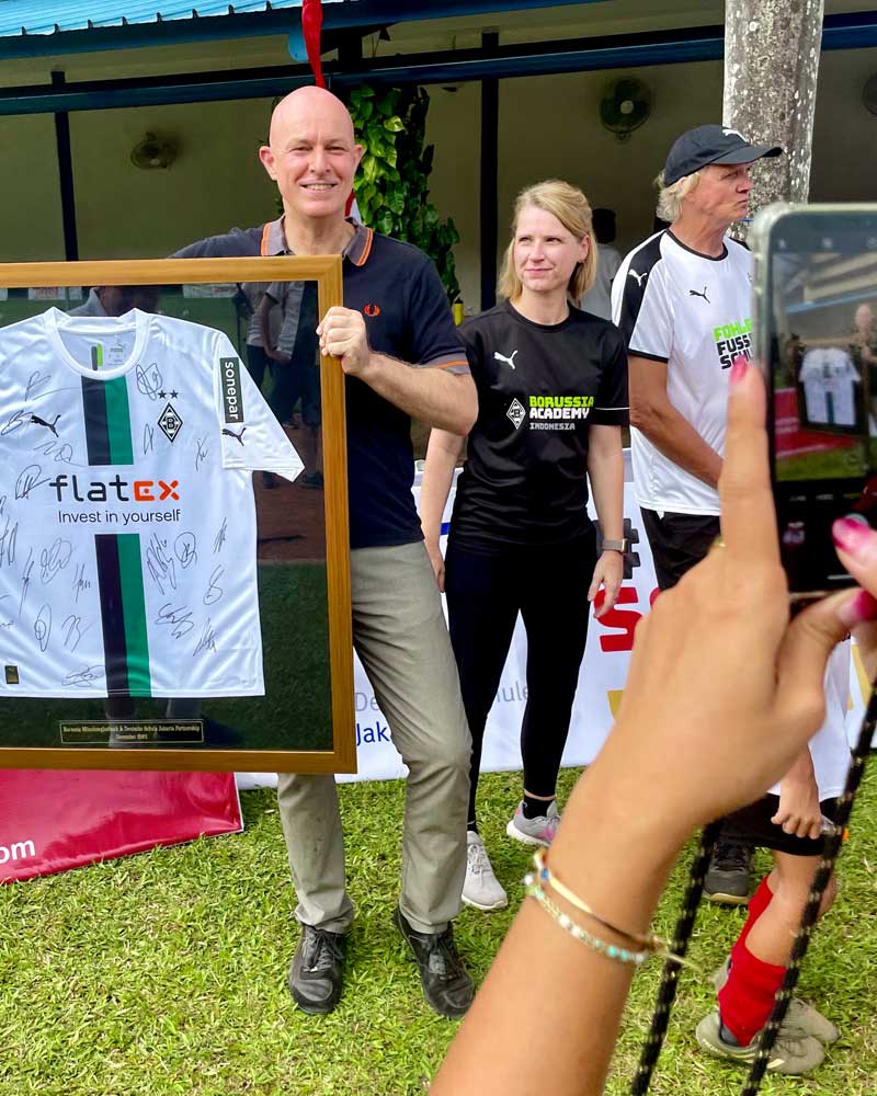 A man is holding a framed shirt that says flatex on it.