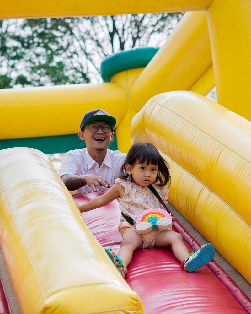 A man and a little girl are playing on an inflatable slide.
