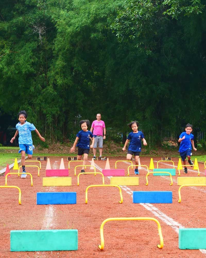 A group of children are running through hurdles on a track.