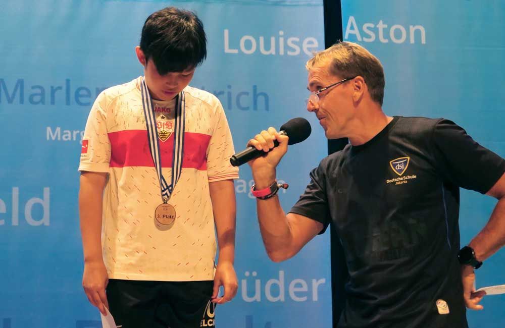 A man is talking into a microphone next to a boy with a medal around his neck