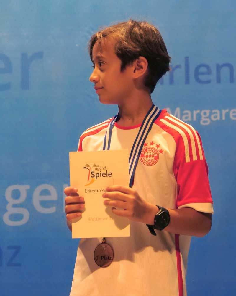 A young boy wearing a medal and holding a piece of paper that says