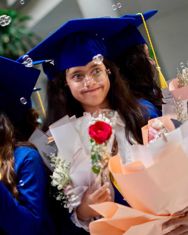 A girl in a graduation cap and gown is holding a bouquet of flowers.