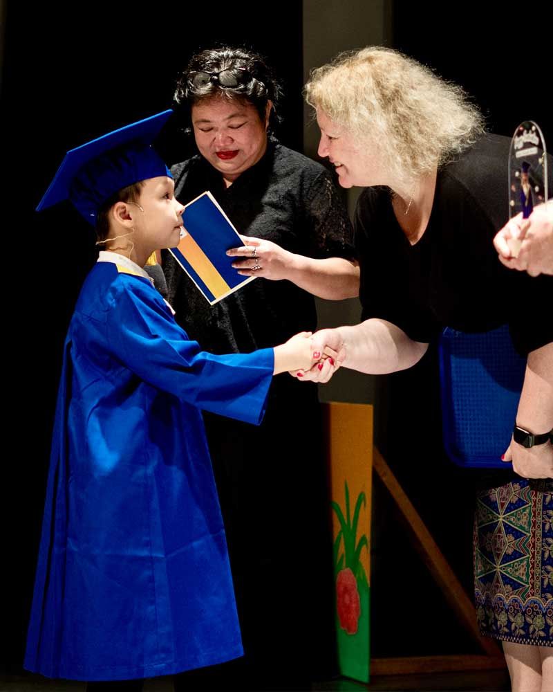 A little girl in a graduation cap and gown shakes hands with a woman