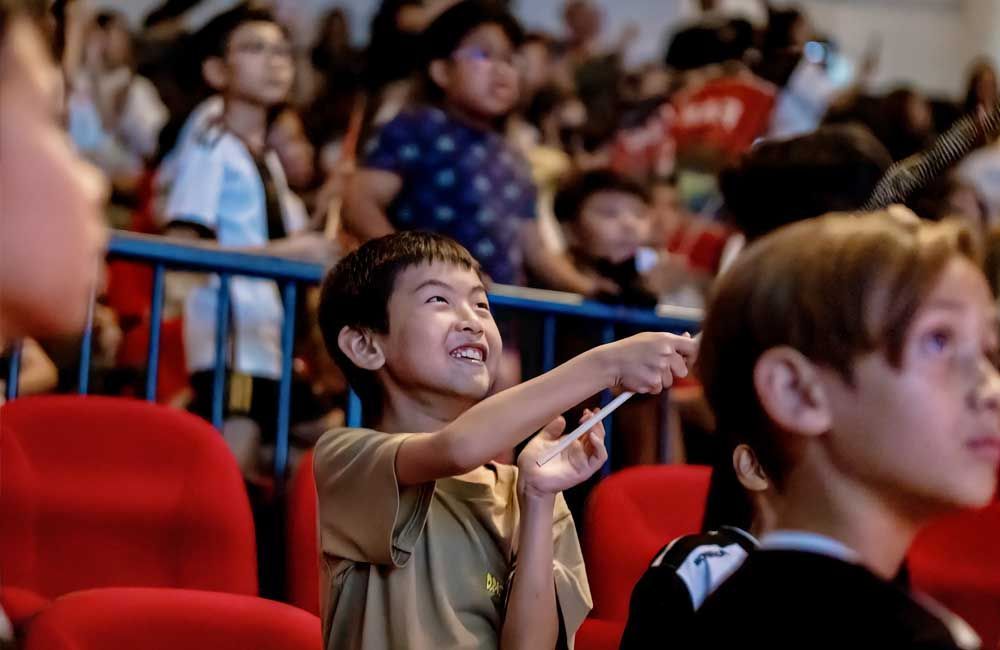 A group of children are sitting in red seats in a theater.
