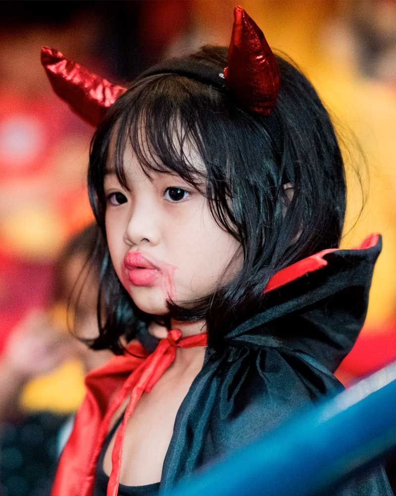 A little girl wearing devil horns and a cape