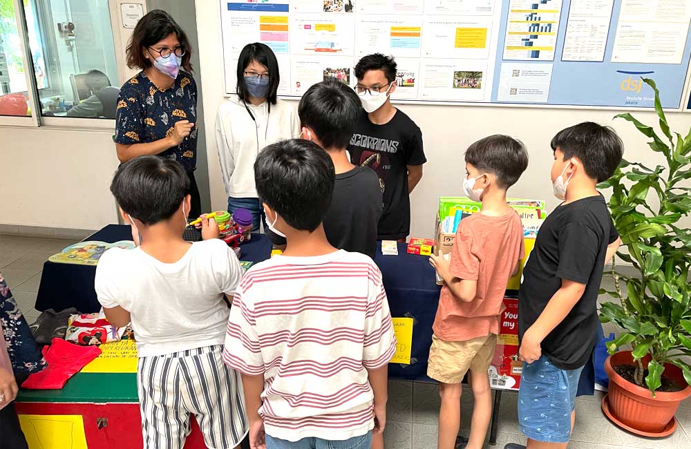 A group of children wearing face masks are standing around a table.