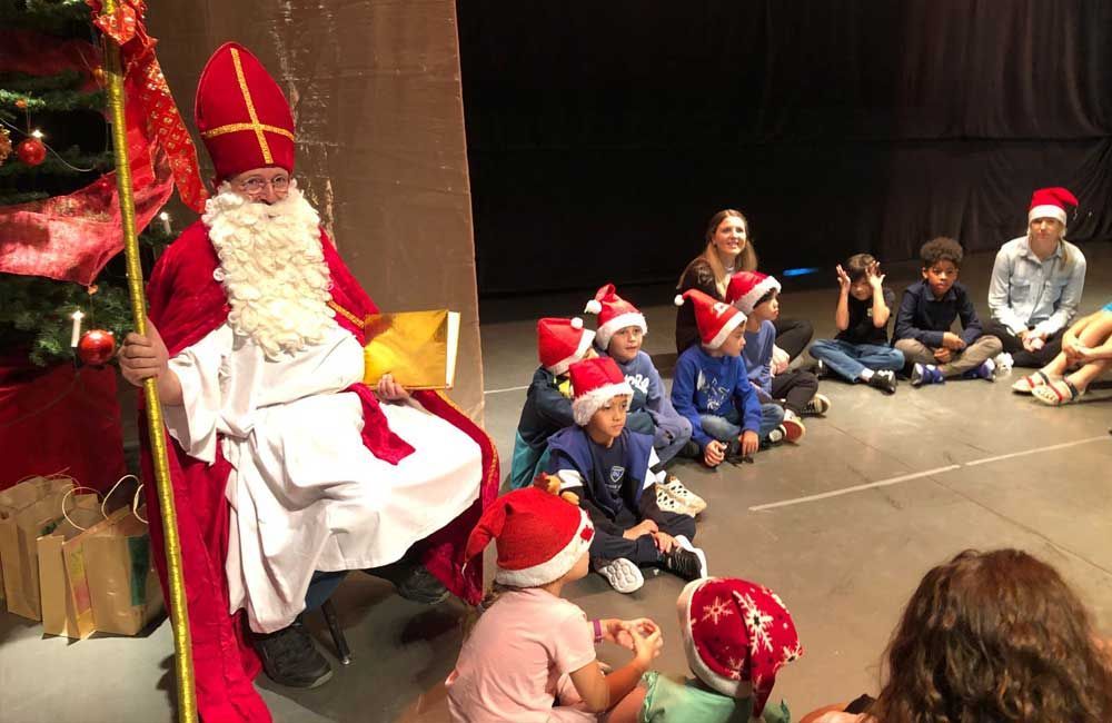 A group of children are sitting on the floor next to a man dressed as santa claus.
