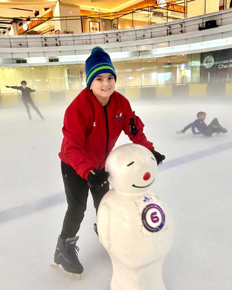 A young boy is standing next to a snowman on an ice rink.