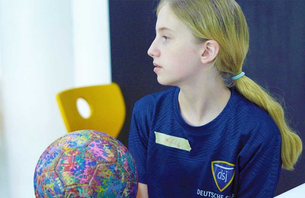 A young girl in a blue shirt is holding a colorful ball.