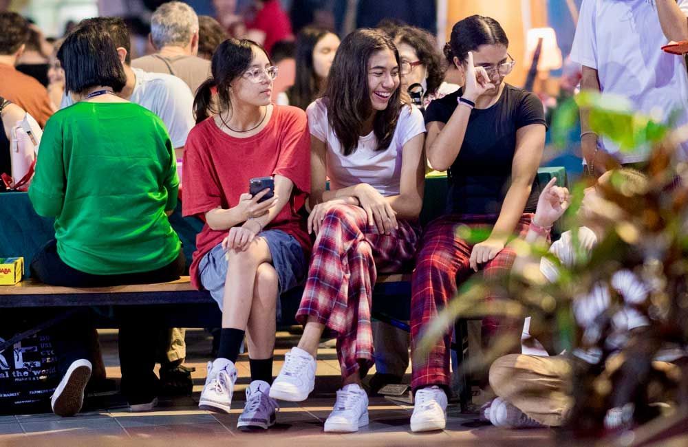 A group of people are sitting on a bench talking to each other.