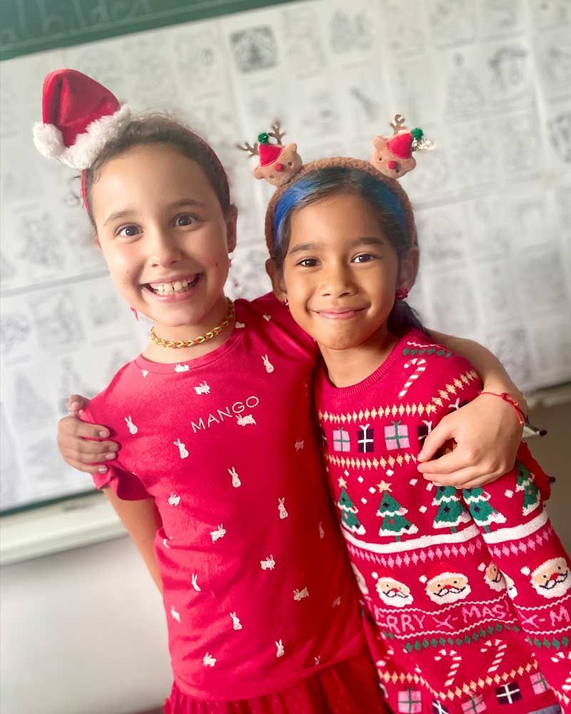 Two young girls wearing christmas sweaters are posing for a picture