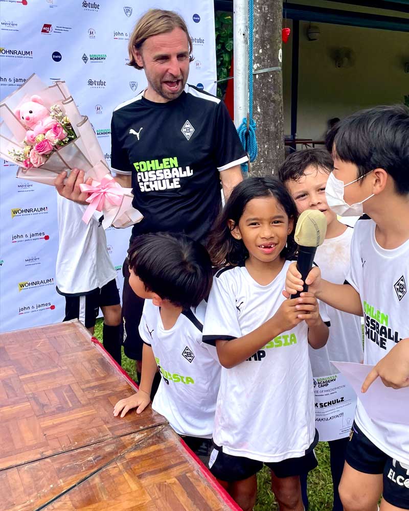 A man is holding a bouquet of flowers while standing next to a group of children.