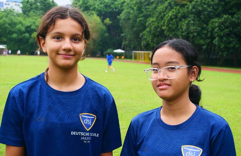 Two young girls wearing blue shirts are standing next to each other on a field.