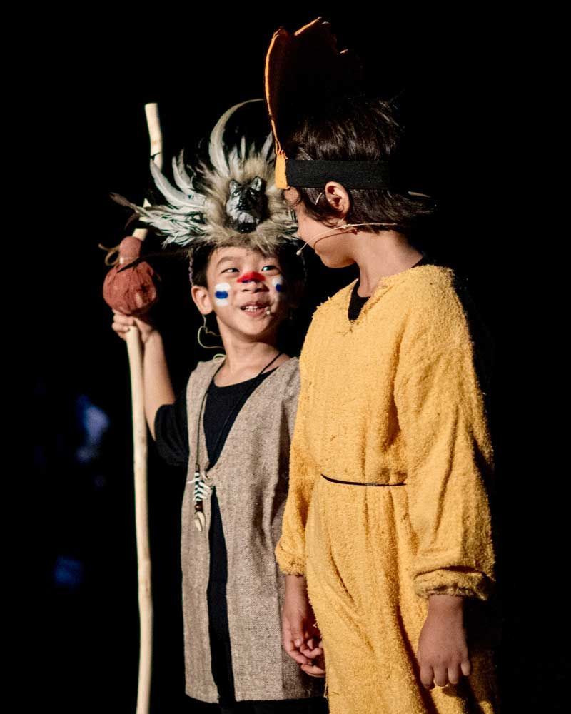 Two children dressed in native american costumes are standing next to each other on a stage.