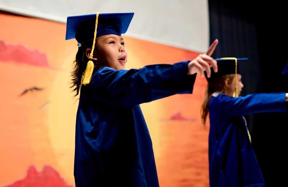 A girl in a graduation cap and gown is pointing at something.