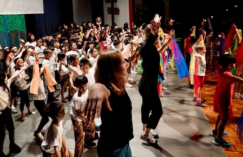 A woman is standing in front of a group of children dancing on a stage.