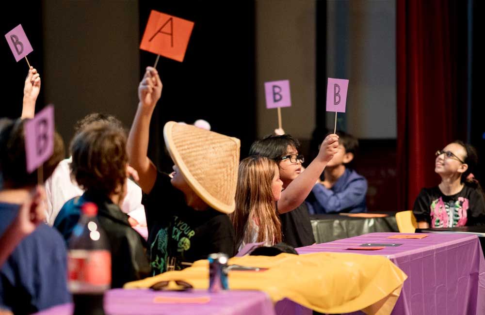 A group of children are sitting at a table holding up signs with letters on them.