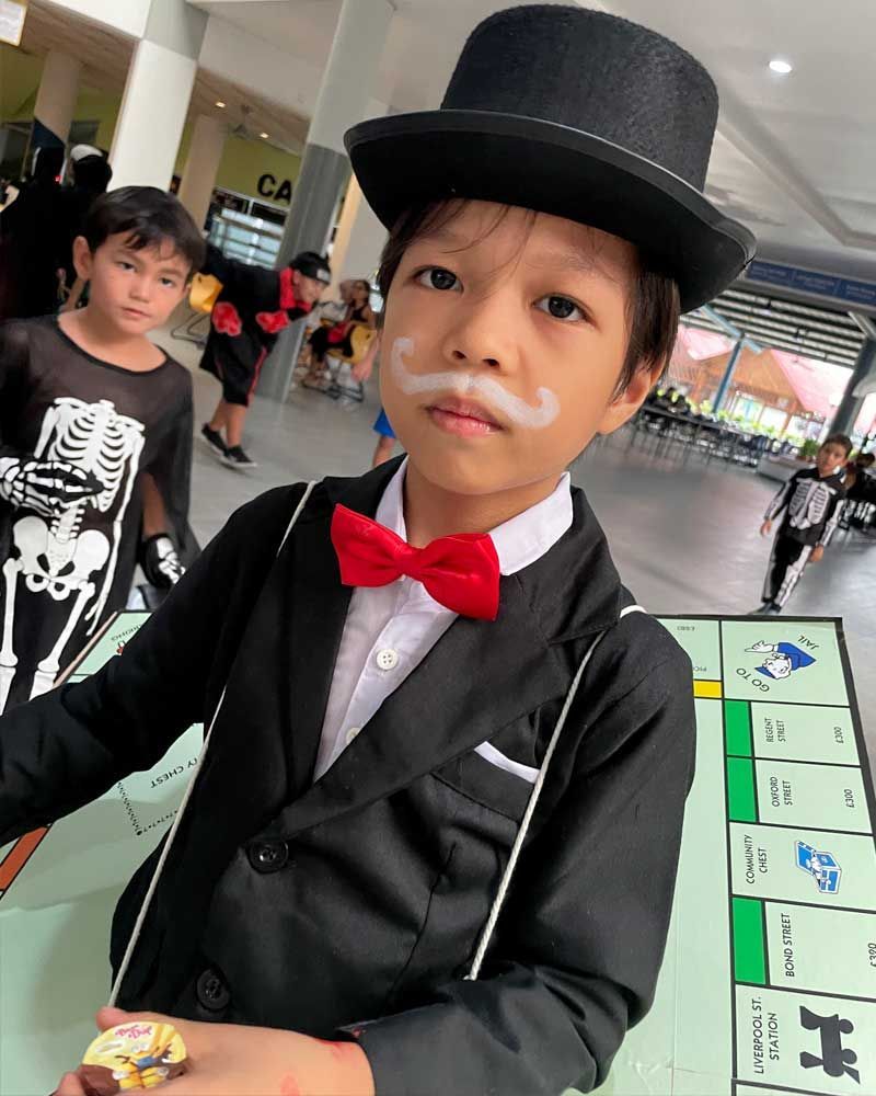 A young boy in a top hat and bow tie is playing monopoly.