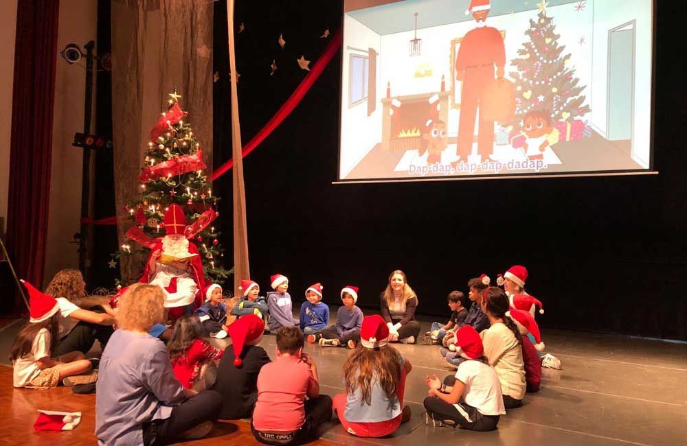 A group of children are sitting on the floor in front of a projector screen watching a christmas movie.