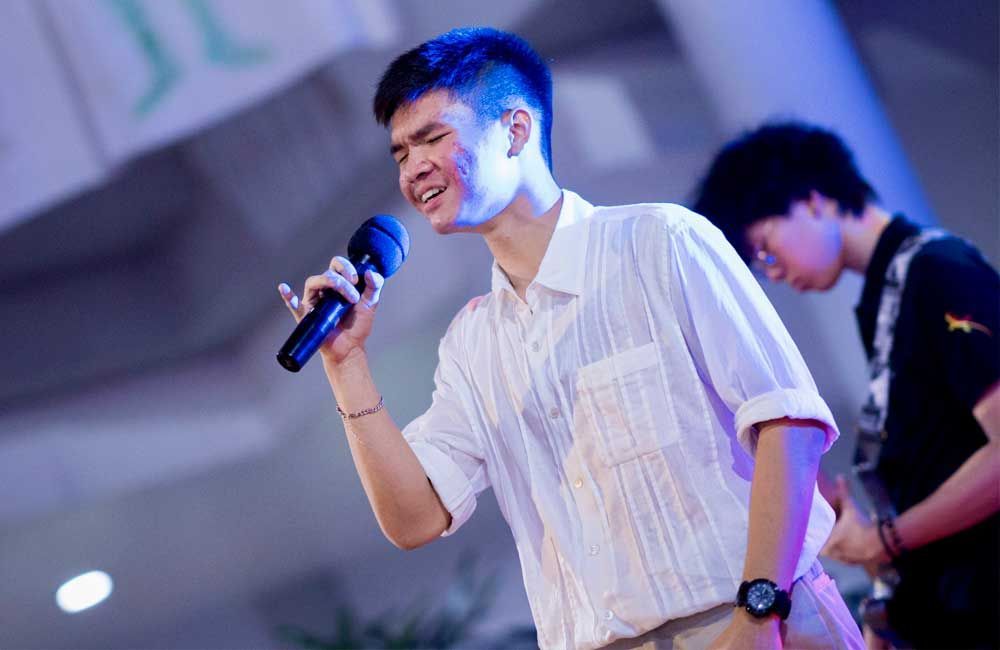 A young man is singing into a microphone on a stage.