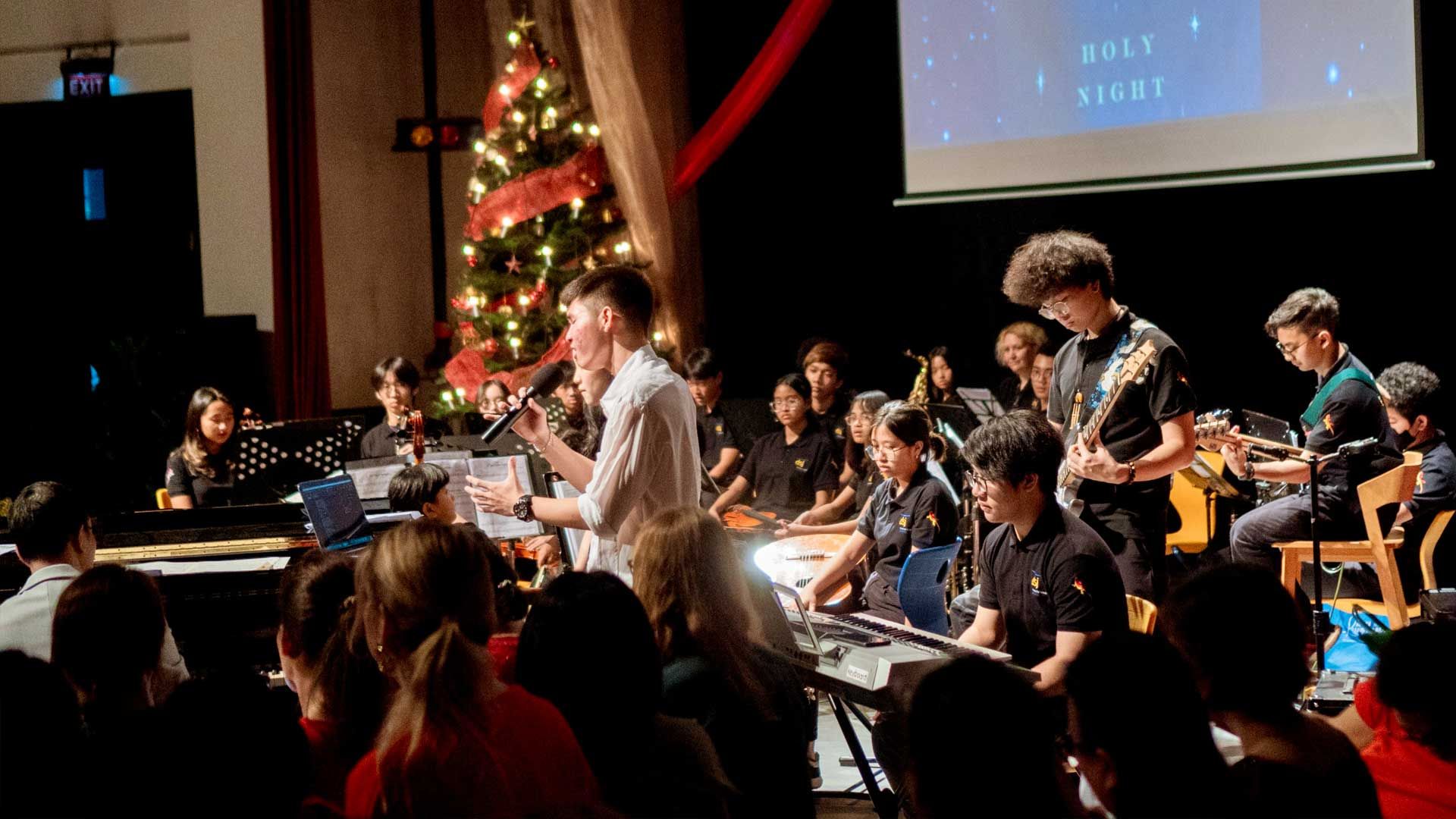 a school student orchestra  playing instruments in front of a christmas tree