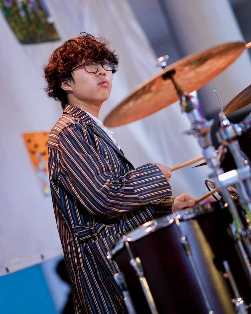A young man in a striped suit is playing drums