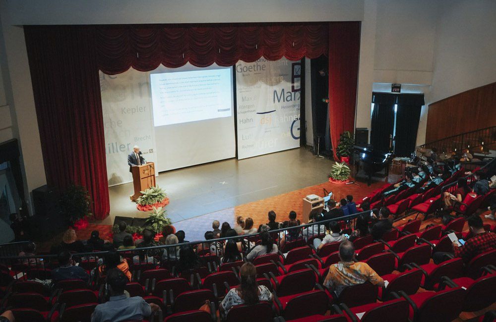 A man is giving a presentation in front of a large audience in an auditorium.