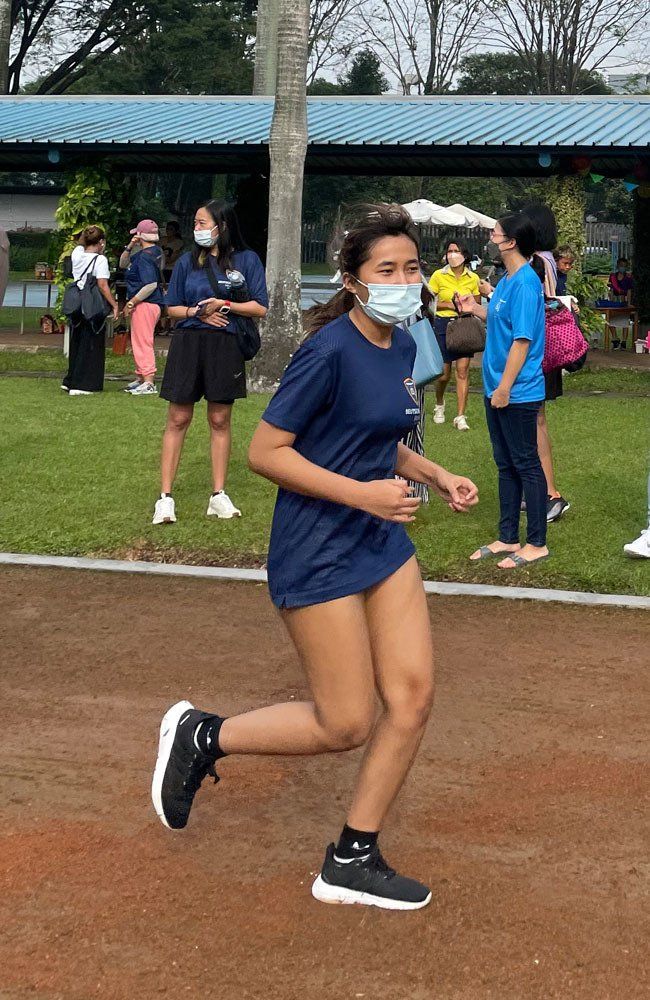 A woman wearing a mask is running on a track.