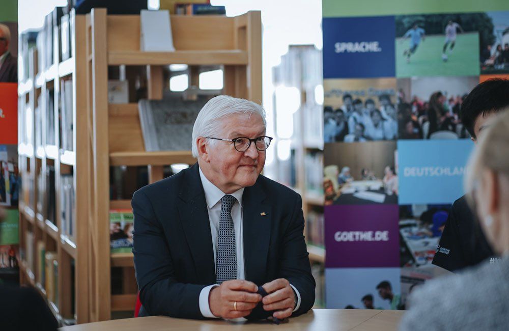 A man in a suit and tie is sitting at a table in a library.