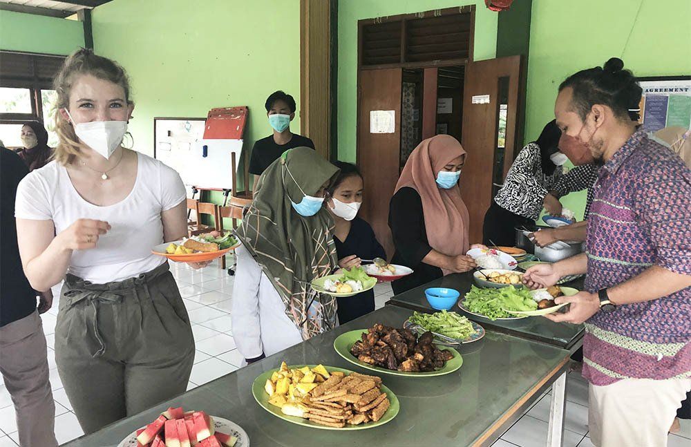 A group of people wearing face masks are standing around a table with plates of food.