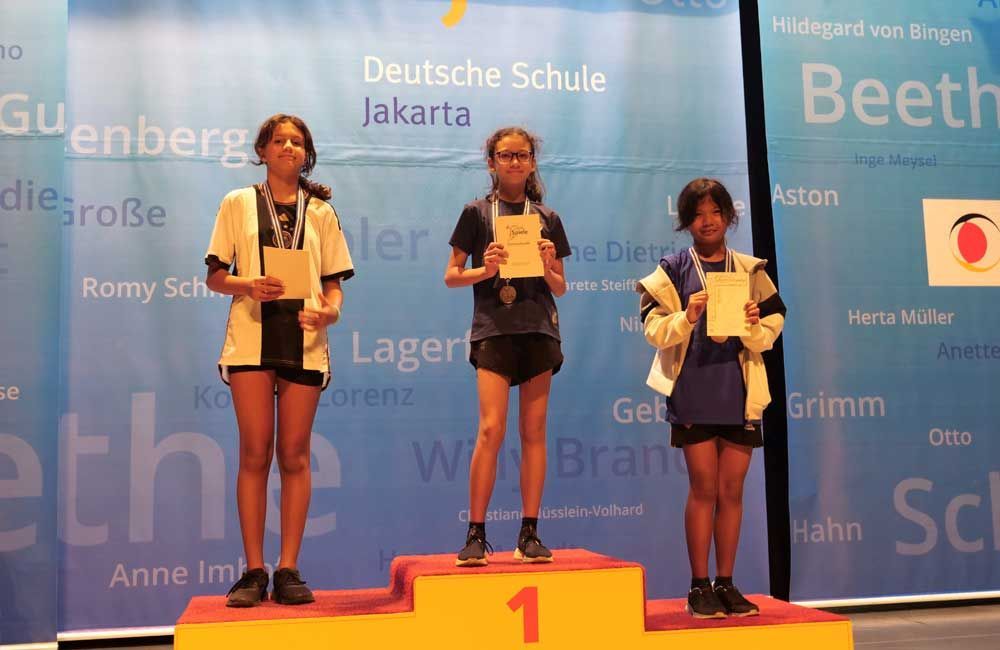 Three girls are standing on a podium with the number 1 on it
