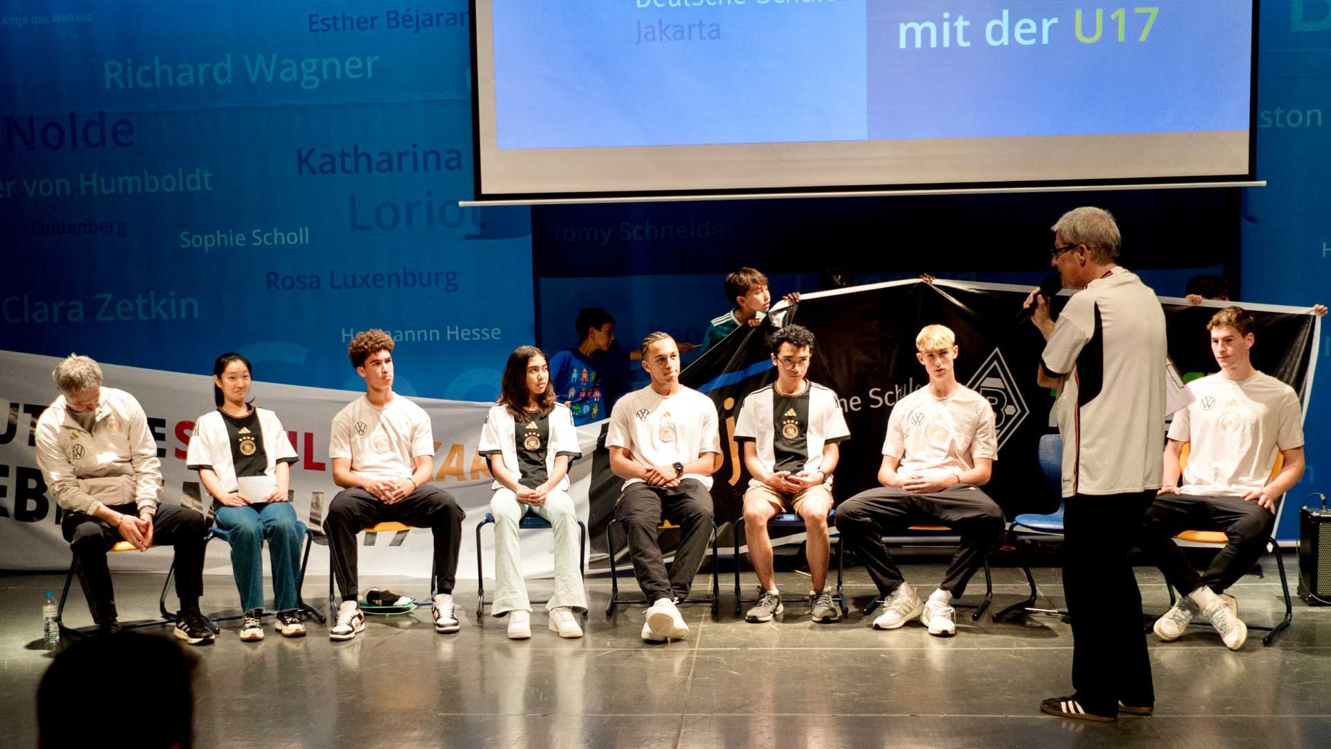 A woman is standing on a stage talking to a group of people sitting in chairs.