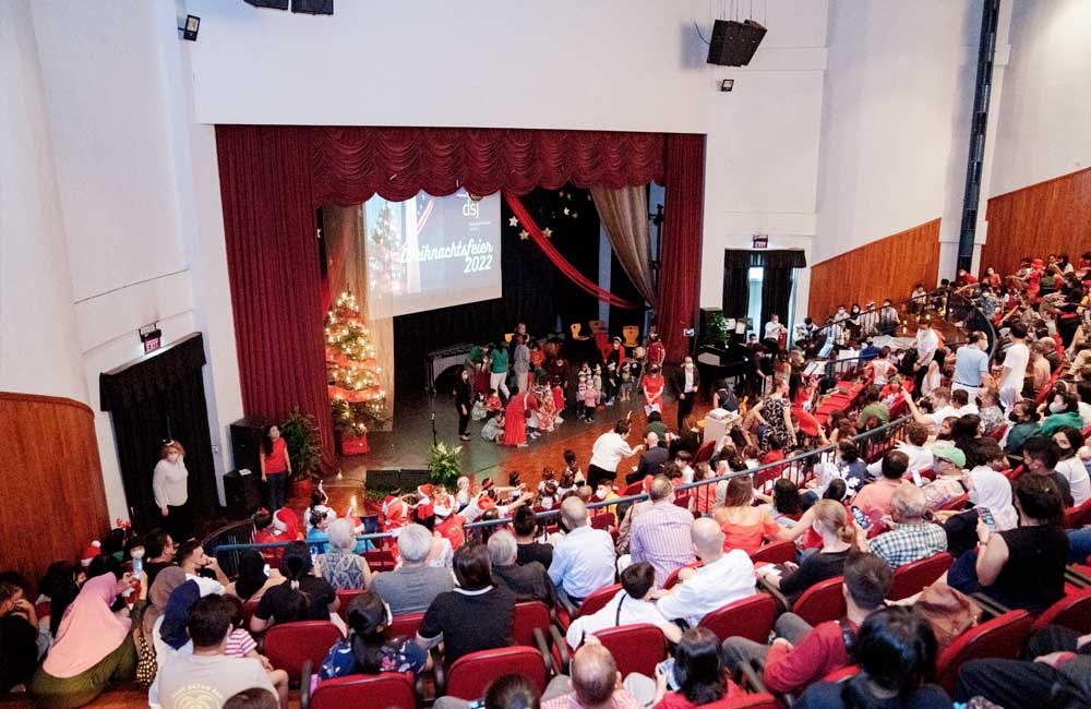 A large group of people are sitting in a large auditorium watching a christmas concert.