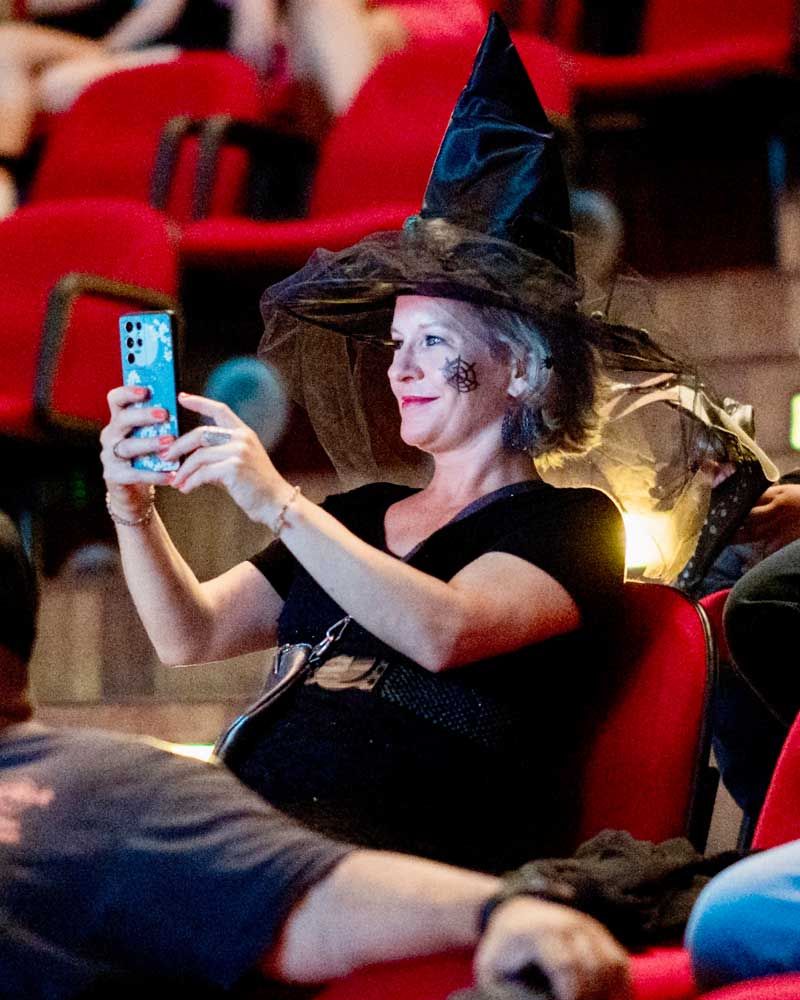 A woman in a witch hat is taking a picture with her phone