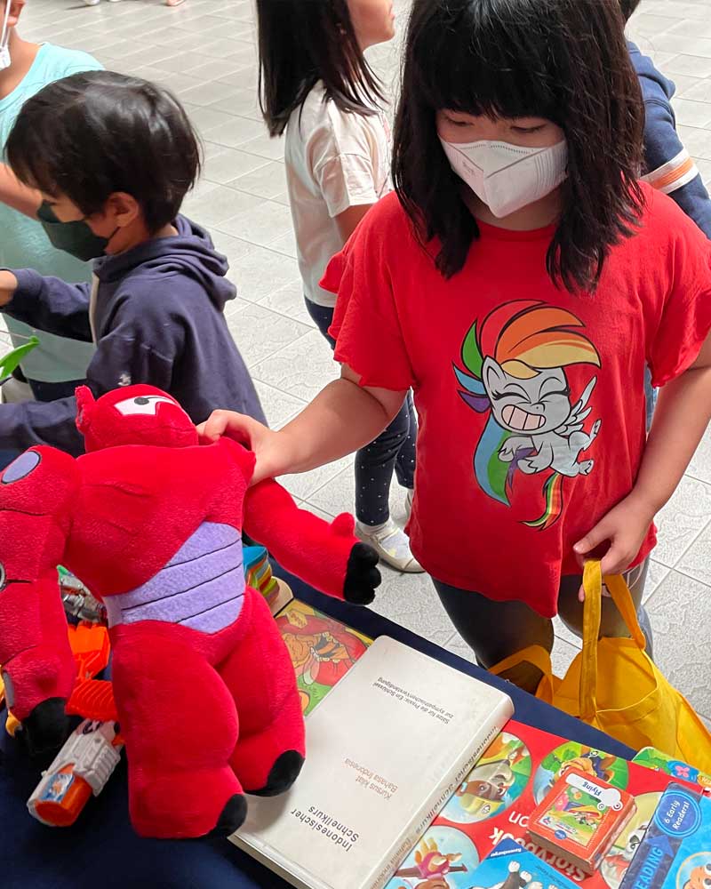 A girl wearing a mask is holding a stuffed animal next to a book.