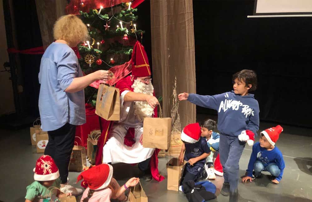 A group of children are playing with santa claus in front of a christmas tree.