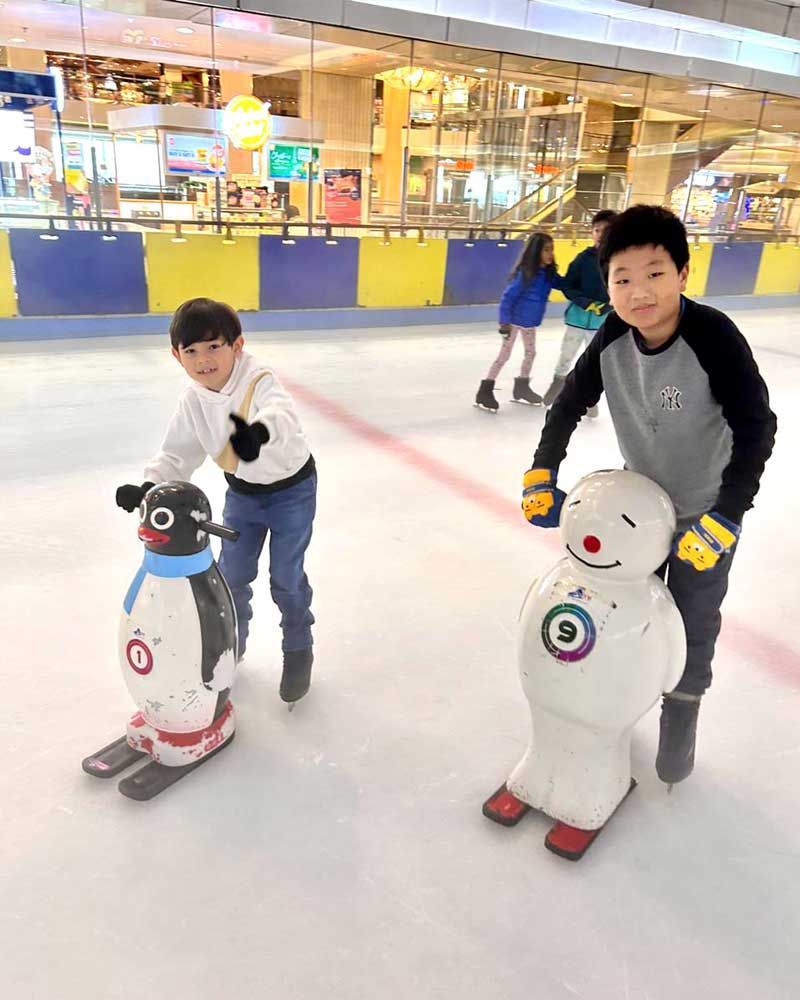 Two young boys are riding penguins and snowmen on an ice rink.