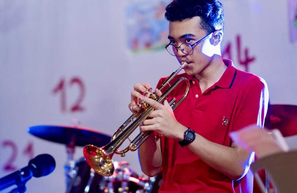 A young man in a red shirt is playing a trumpet on stage.