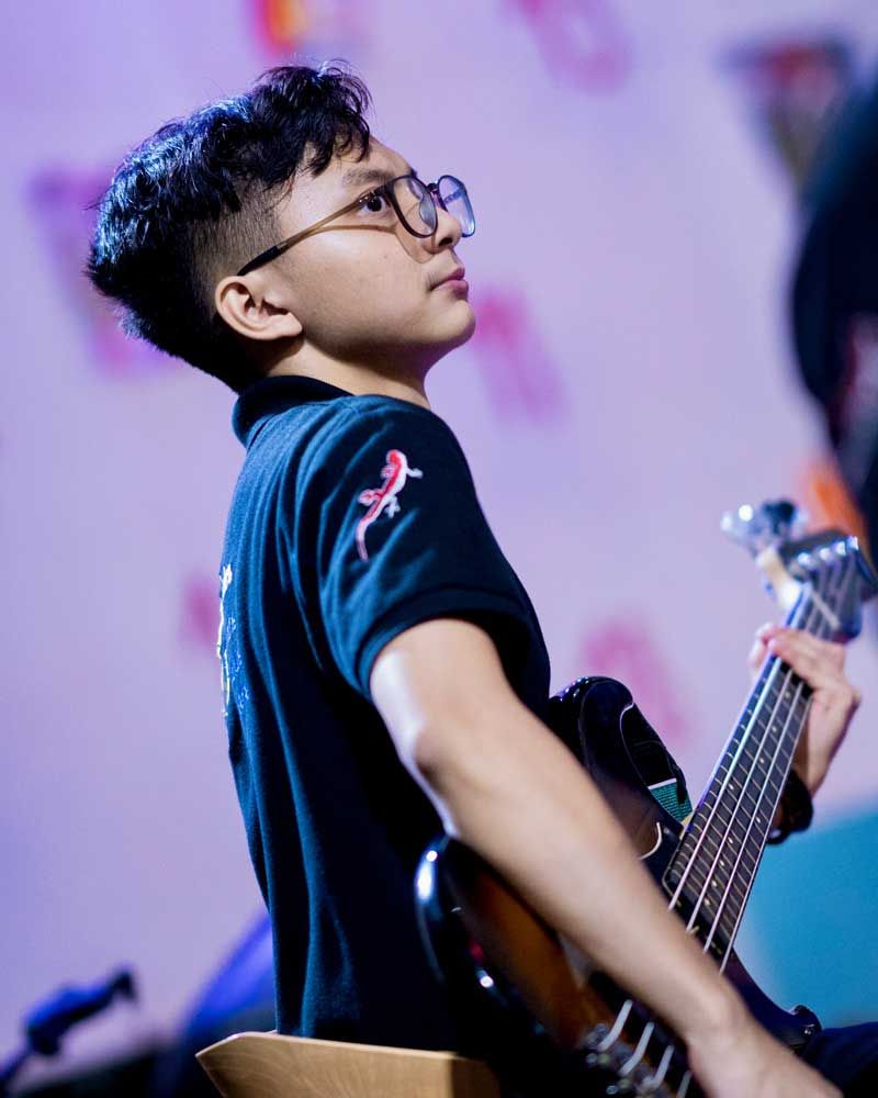 A young man wearing glasses is playing a guitar