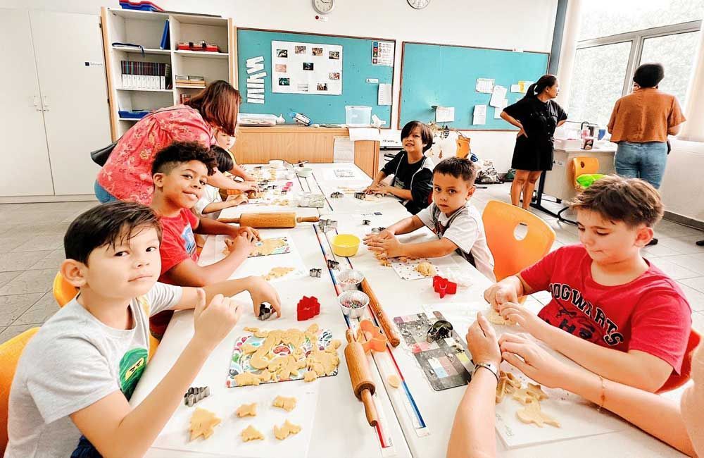 A group of children are sitting at a table in a classroom making cookies.