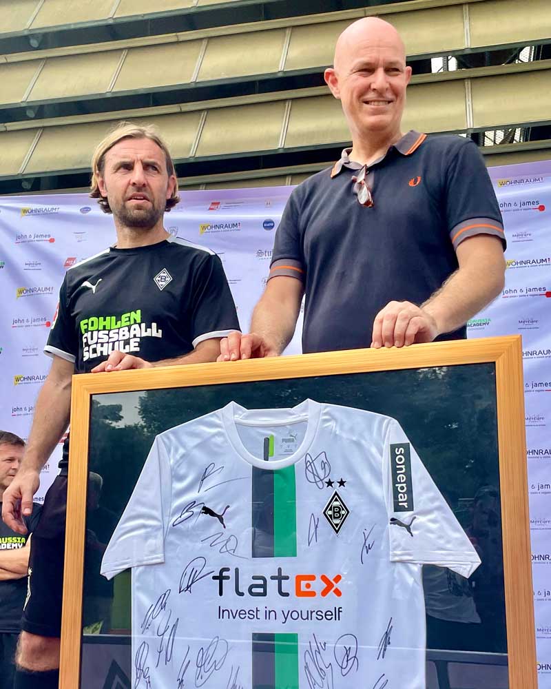 Two men are standing next to each other holding a signed soccer jersey.