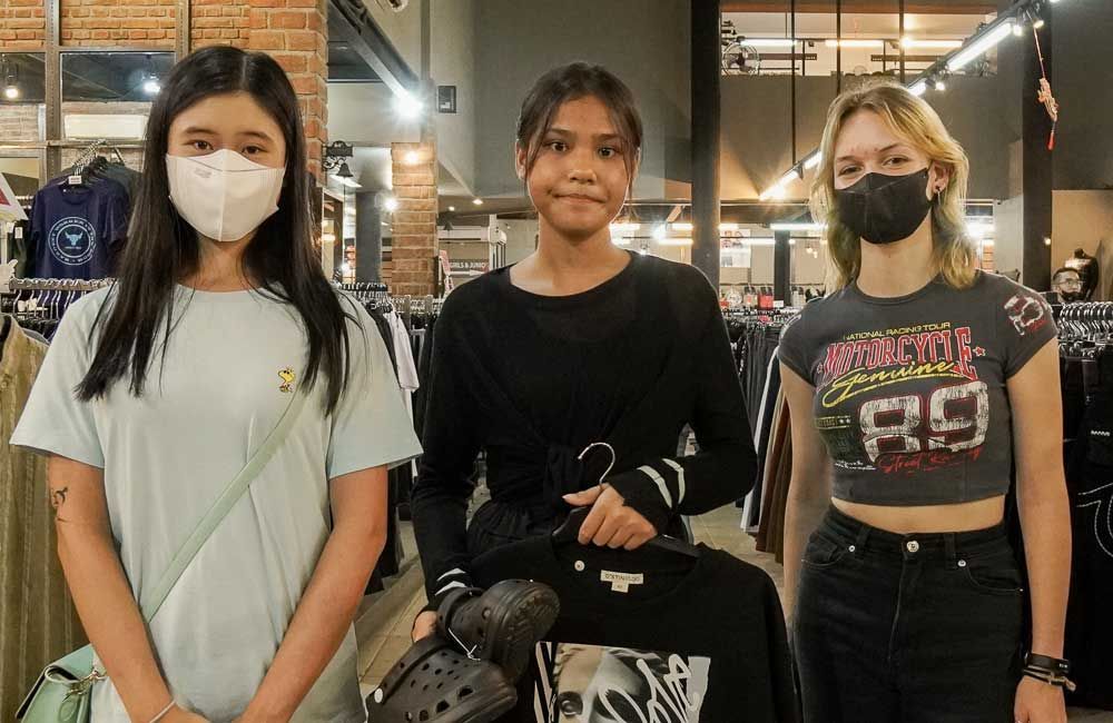 Three girls wearing face masks are standing next to each other in a clothing store.